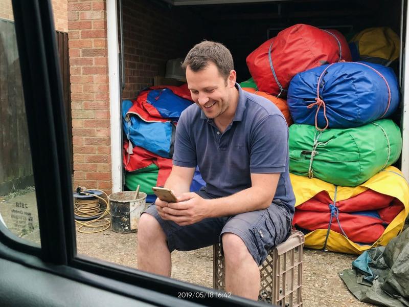 A bouncy castle hire operator smiling at a new booking notification on their phone in their storage yard