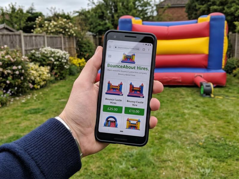 A bouncy castle hire website shown on a phone screen held outdoors near a castle
