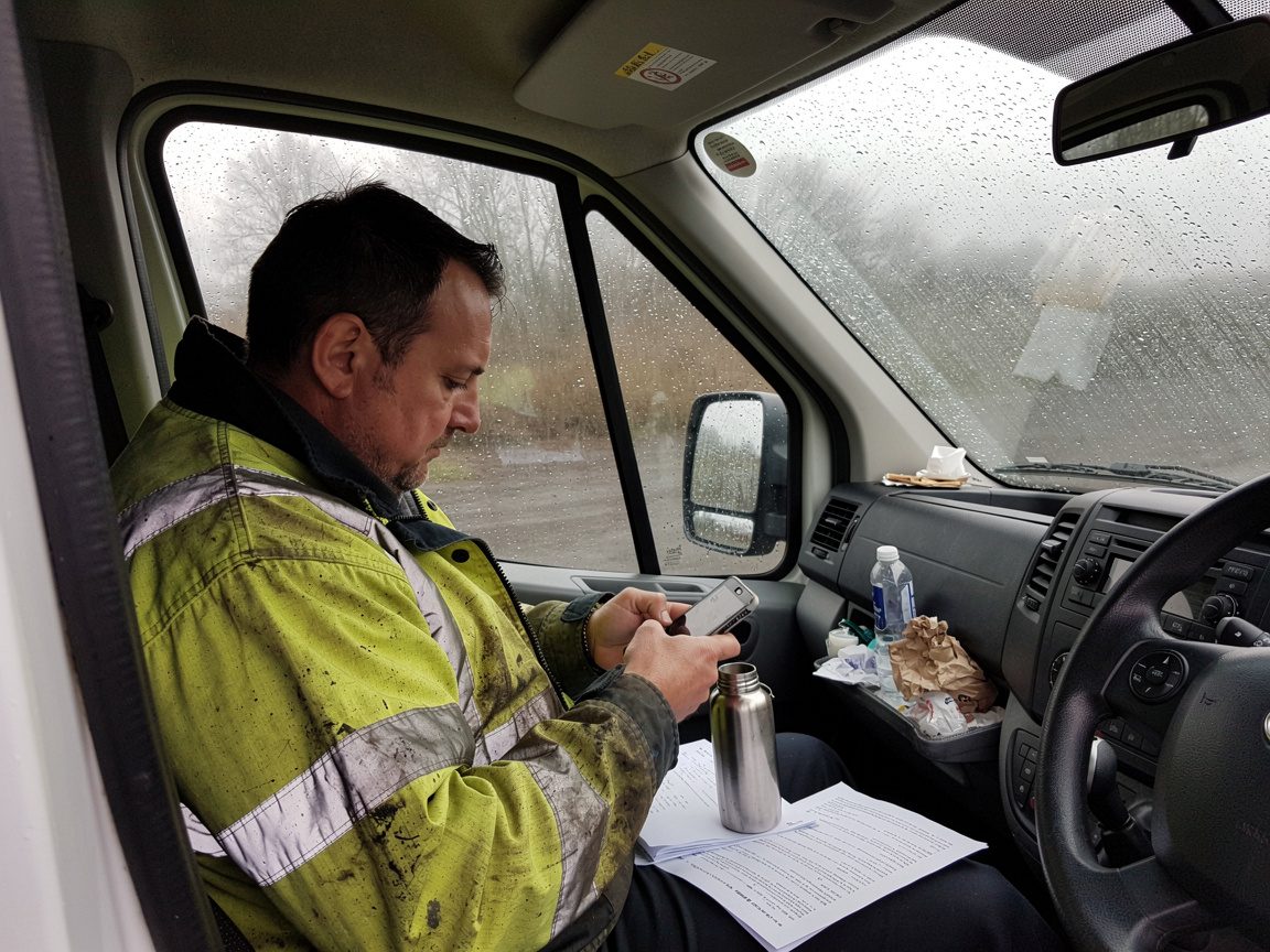 A landscaper smiling at a new customer enquiry on his phone while in his van