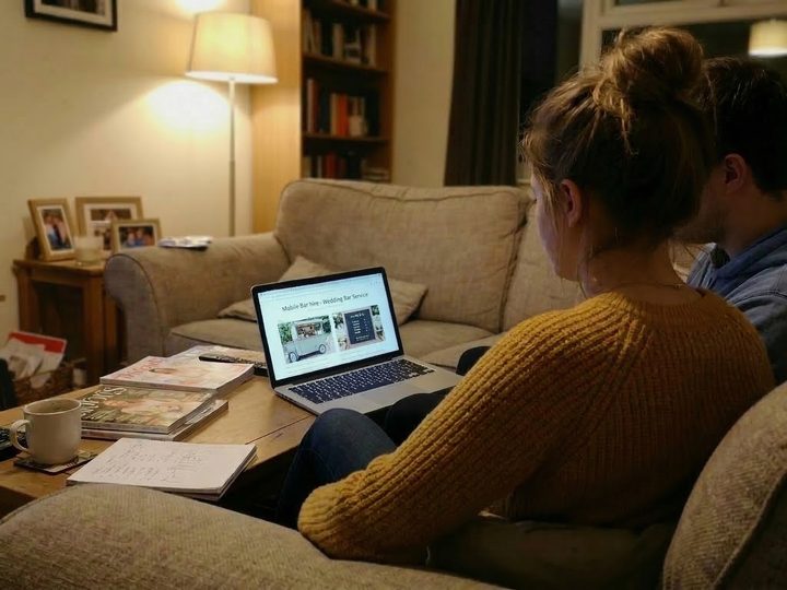 A couple at a kitchen table researching mobile bar hire for their wedding on a laptop