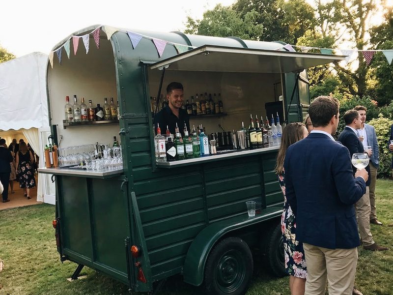 A converted horsebox bar set up at an outdoor wedding with guests around it
