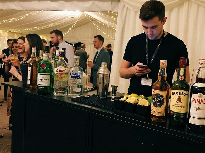 A modular bar setup inside a wedding marquee with bottles and glassware displayed