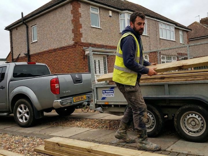 A builder loading timber onto a flatbed trailer in a hire yard