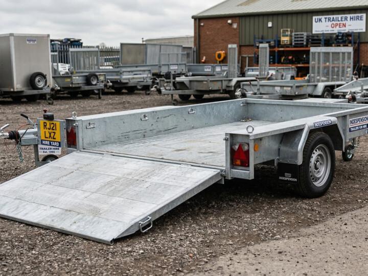 Galvanised flatbed trailer with folding ramp lowered in a UK hire yard
